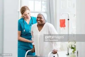Une infirmière à domicile confiante aide une femme âgée à utiliser un déambulateur pendant son rétablissement en raison d'un AVC. La patiente sourit des progrès qu'elle fait pendant sa convalescence.